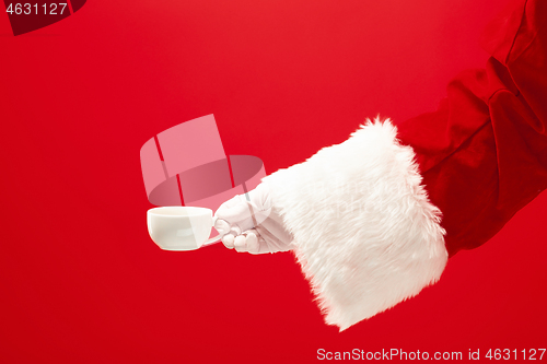 Image of Christmas coffee. The Santa hand holding cup of cofee isolated on a red background with space for text