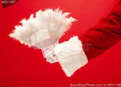 Image of Hand of Santa Claus holding a toy Christmas retro fan on red background