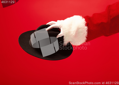 Image of Hand of Santa Claus holding a male hat on red background