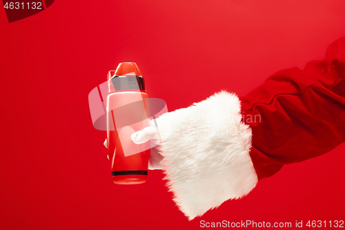 Image of Christmas coffee. The Santa hand holding thermos of cofee isolated on a red background with space for text