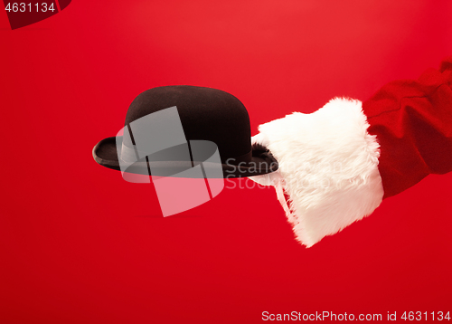 Image of Hand of Santa Claus holding a male hat on red background