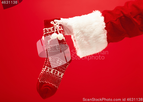 Image of Hand of Santa Claus holding a Christmas Knitted Socks on red background