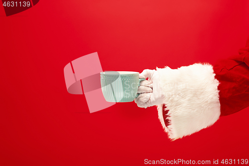 Image of Christmas coffee. The Santa hand holding cup of cofee isolated on a red background with space for text