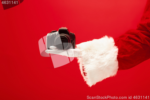 Image of Hand of Santa Claus holding a camera on red background