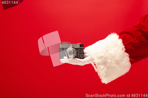 Image of Hand of Santa Claus holding a camera on red background