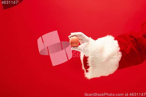 Image of Hand of Santa Claus holding an egg on red background