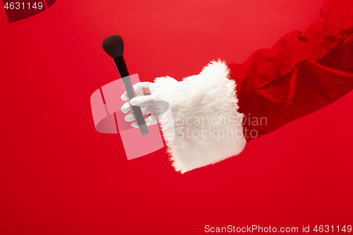 Image of Hand of Santa Claus holding a makeup brush for powder on red background