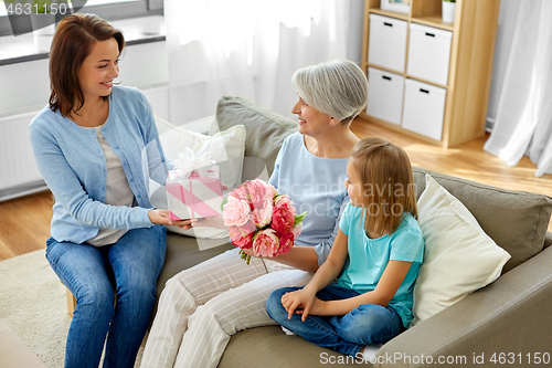 Image of family giving present and flowers to grandmother
