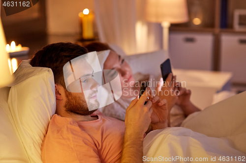 Image of couple using smartphones in bed at night
