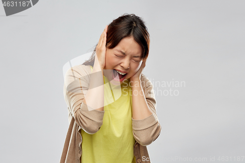 Image of stressed asian woman closing ears and screaming