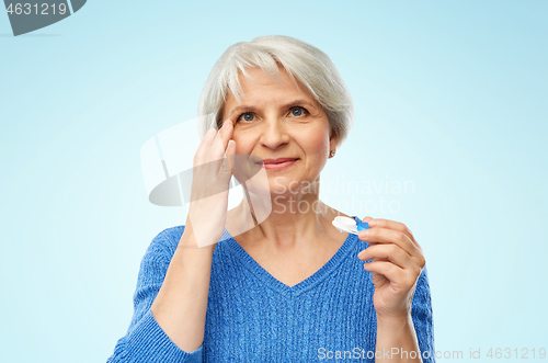 Image of senior woman applying contact lenses over blue