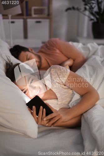 Image of woman using smartphone while boyfriend is sleeping