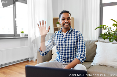 Image of indian male blogger waving hand at home