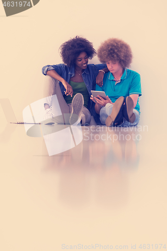 Image of multiethnic couple sitting on the floor with a laptop and tablet