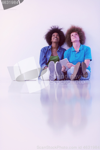 Image of multiethnic couple sitting on the floor with a laptop and tablet
