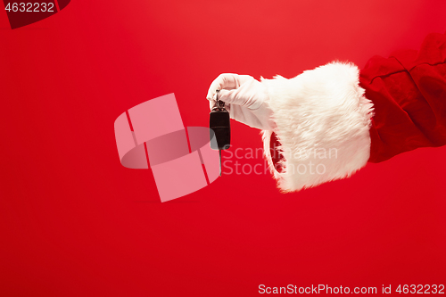 Image of Hand of Santa Claus holding a gift on red background