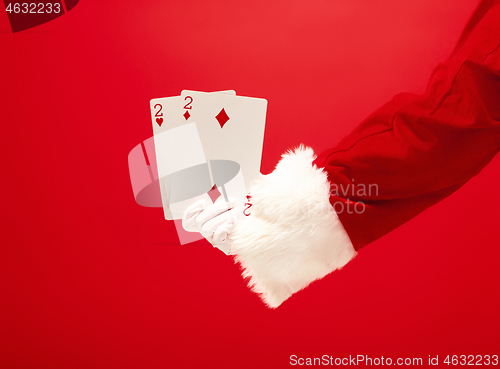 Image of Hand of Santa Claus holding a playing cards on red background