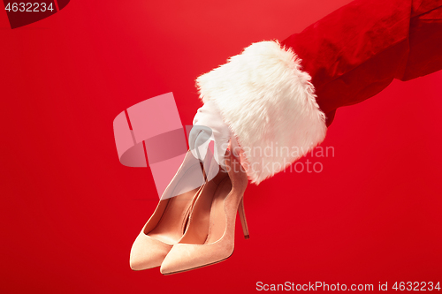 Image of Hand of Santa Claus holding a women\'s shoes on red background