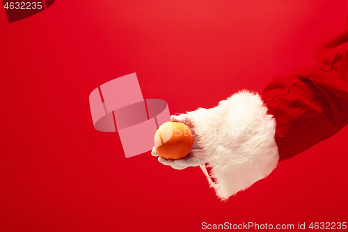 Image of Hand of Santa Claus holding an orange on red background