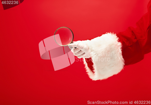 Image of Hand of Santa Claus holding a magnifier on red background