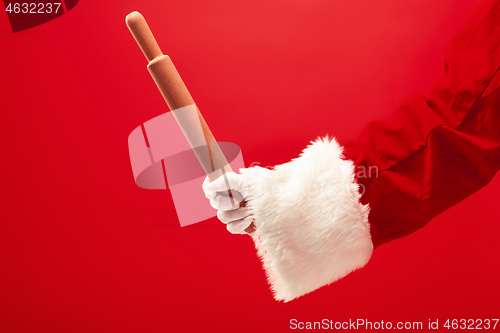 Image of Hand of Santa Claus holding a culinary rolling pin on red background