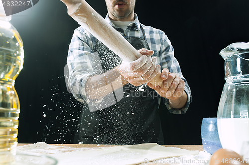 Image of Professional male cook sprinkles dough with flour, preapares or bakes bread at kitchen table