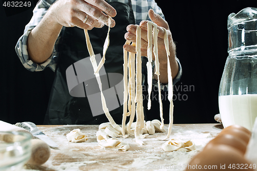 Image of Professional male cook sprinkles dough with flour, preapares or bakes bread at kitchen table