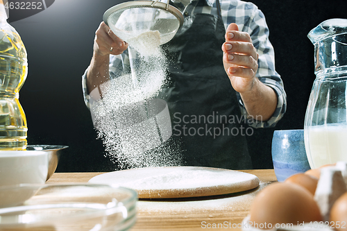 Image of Professional male cook sprinkles dough with flour, preapares or bakes bread at kitchen table