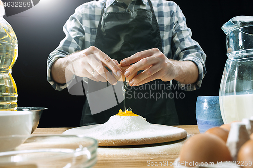 Image of Professional male cook sprinkles dough with flour, preapares or bakes bread at kitchen table