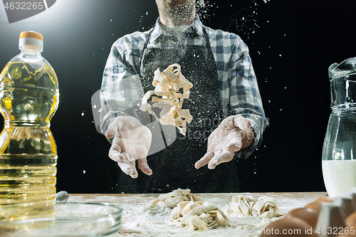 Image of Professional male cook sprinkles dough with flour, preapares or bakes bread at kitchen table