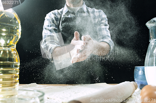 Image of Professional male cook sprinkles dough with flour, preapares or bakes bread at kitchen table