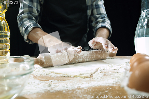 Image of Professional male cook sprinkles dough with flour, preapares or bakes bread at kitchen table