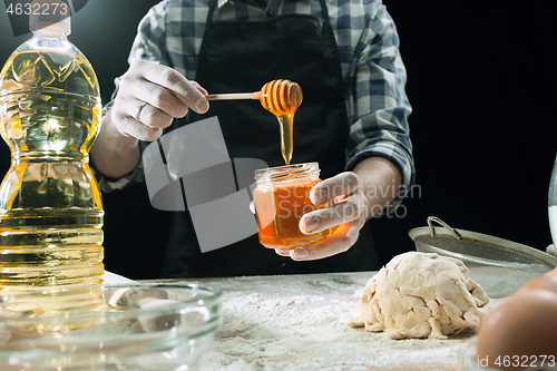 Image of Professional male cook sprinkles dough with flour, preapares or bakes bread at kitchen table