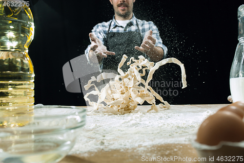 Image of Professional male cook sprinkles dough with flour, preapares or bakes bread at kitchen table