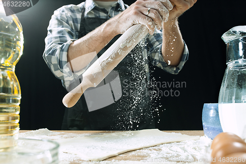 Image of Professional male cook sprinkles dough with flour, preapares or bakes bread at kitchen table