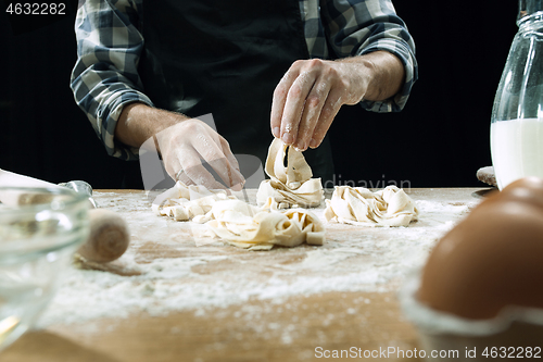 Image of Professional male cook sprinkles dough with flour, preapares or bakes bread at kitchen table