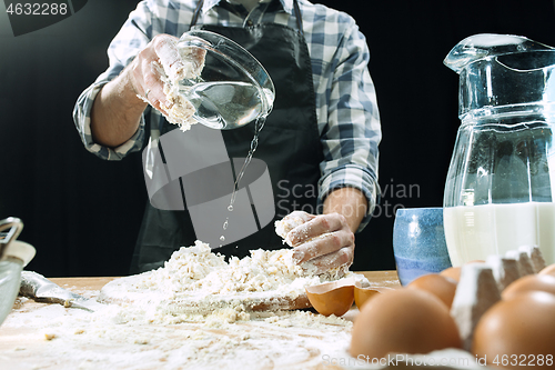 Image of Professional male cook sprinkles dough with flour, preapares or bakes bread at kitchen table