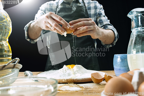 Image of Professional male cook sprinkles dough with flour, preapares or bakes bread at kitchen table