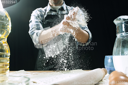 Image of Professional male cook sprinkles dough with flour, preapares or bakes bread at kitchen table