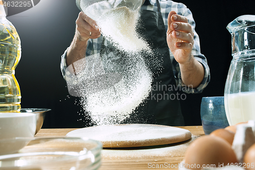 Image of Professional male cook sprinkles dough with flour, preapares or bakes bread at kitchen table