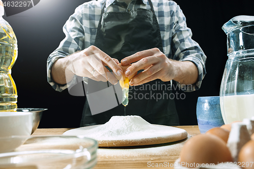 Image of Professional male cook sprinkles dough with flour, preapares or bakes bread at kitchen table