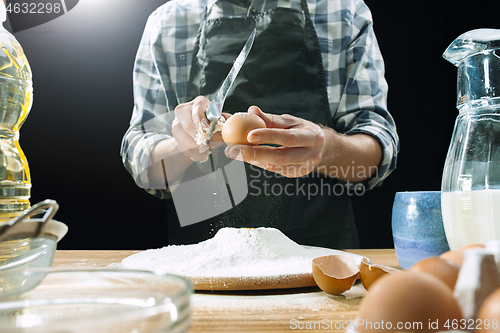 Image of Professional male cook sprinkles dough with flour, preapares or bakes bread at kitchen table