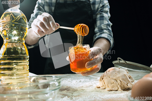 Image of Professional male cook sprinkles dough with flour, preapares or bakes bread at kitchen table