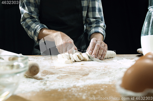 Image of Professional male cook sprinkles dough with flour, preapares or bakes bread at kitchen table