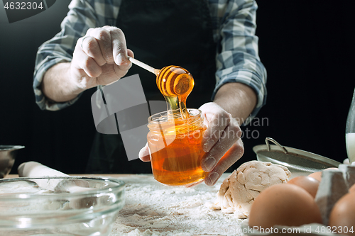 Image of Professional male cook sprinkles dough with flour, preapares or bakes bread at kitchen table