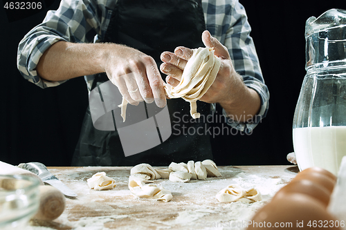 Image of Professional male cook sprinkles dough with flour, preapares or bakes bread at kitchen table