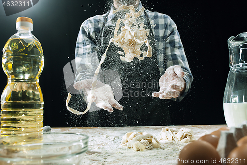 Image of Professional male cook sprinkles dough with flour, preapares or bakes bread at kitchen table