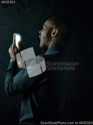 Image of Studio shot of young serious black African man thinking while talking on mobile phone against black background