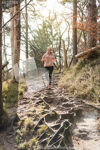 Image of Active sporty woman listening to the music while running in autumn fall forest. Female runner training outdoor. Healthy lifestyle image of young caucasian woman jogging outside