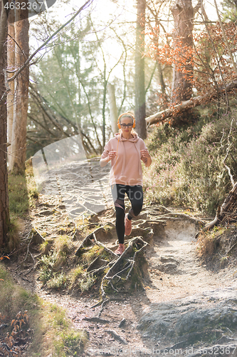 Image of Active sporty woman listening to the music while running in autumn fall forest. Female runner training outdoor. Healthy lifestyle image of young caucasian woman jogging outside